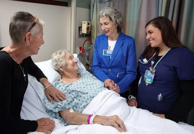 family members and a nurse comfort a patient in a hospital bed